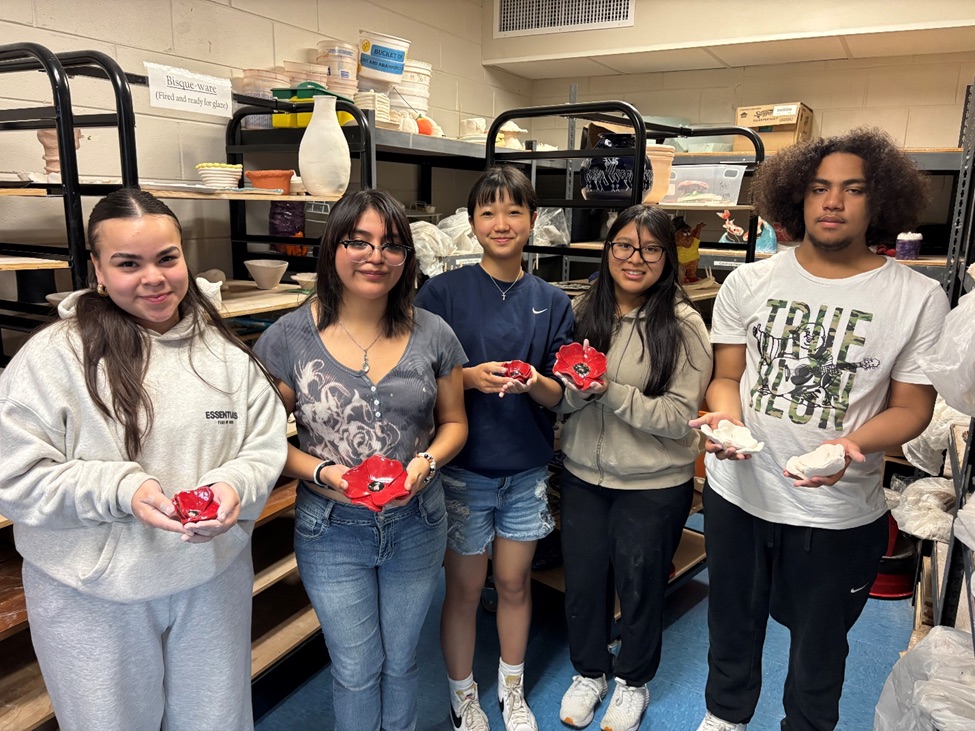 Five students stand in a line holding red ceramic poppies that they crafted.