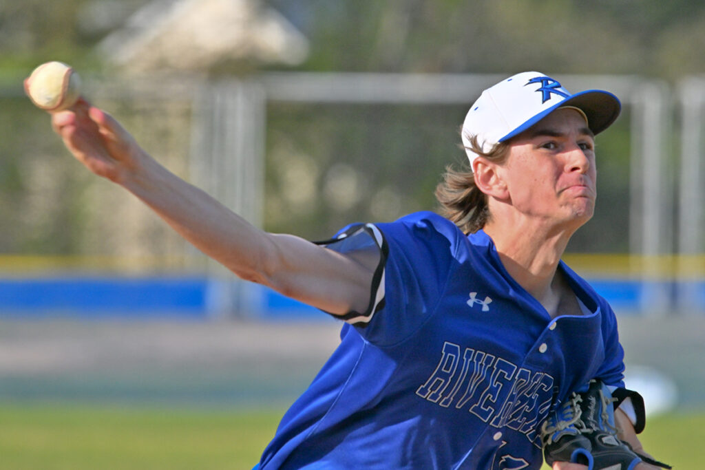 A high school baseball pitcher throws the ball hard, with his face clenched and arm stretched out. He is wearing a white hat.