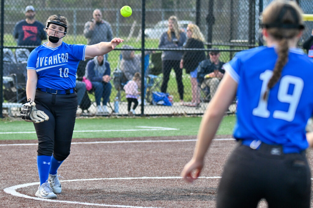Two softball players in blue jerseys and black pants toss the softball back and forth