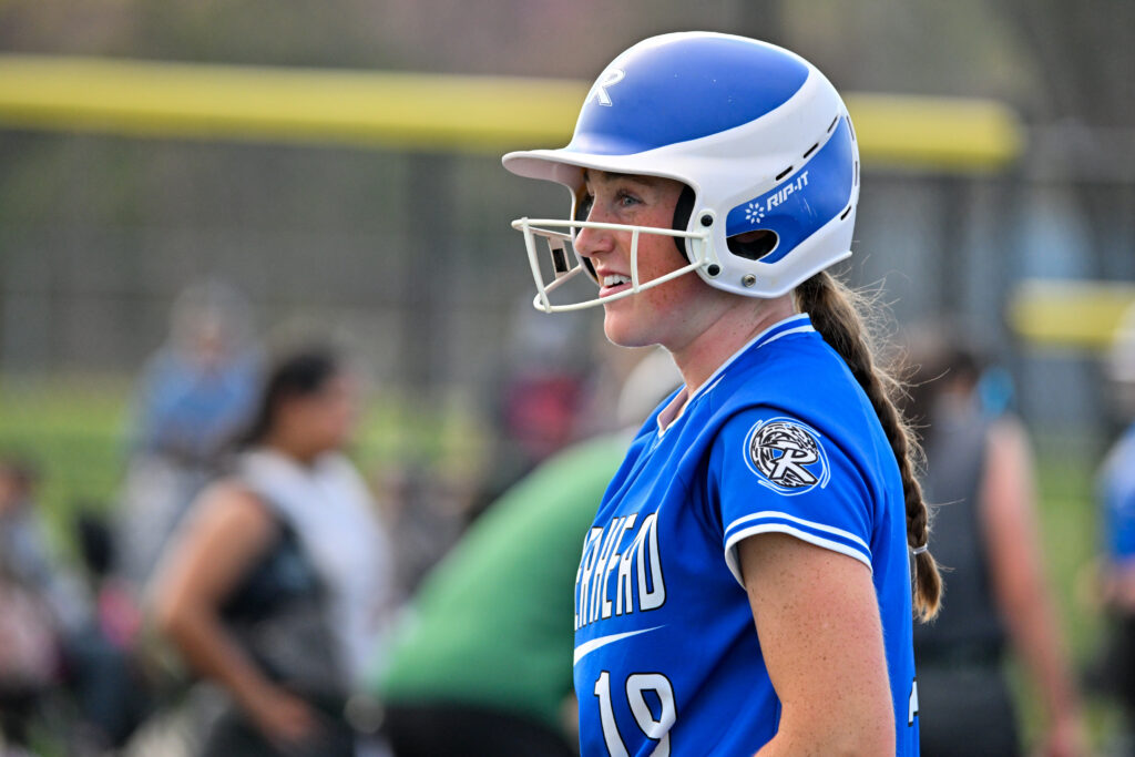 A softball player in a blue jersey and batting helmet stands ready..